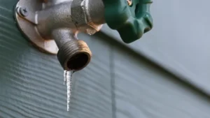 A close up of a frozen outdoor hose bib with an icicle illustrating the importance of preventing water damage during colder seasons