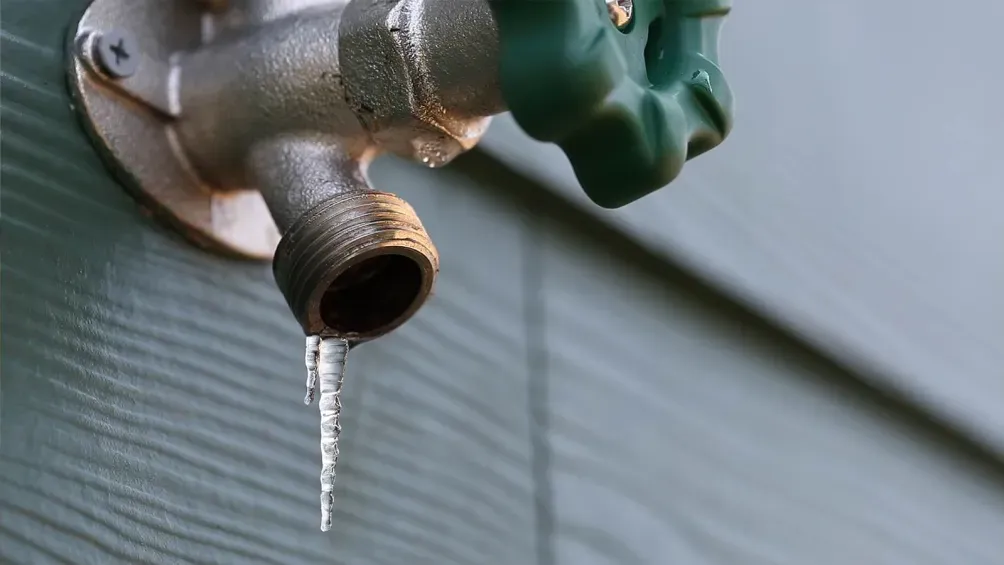 A close-up of a frozen outdoor hose bib with an icicle, illustrating the importance of preventing water damage during colder seasons.