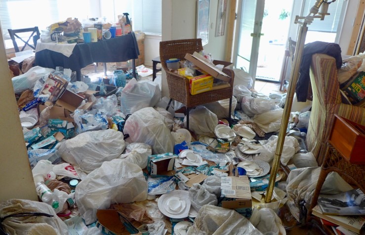 A cluttered and messy living room filled with trash bags paper plates and miscellaneous items illustrating the need for professional hoarding cleanup services by MRC Restoration