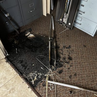 Severe fire damage on a carpeted floor with visible soot and burnt materials near file cabinets.