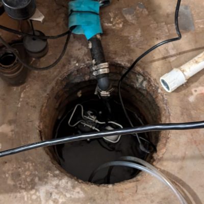 Open sump pump in a basement with visible standing water.