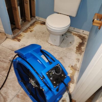 Bathroom floor exposed after water damage with an air mover drying and dehumidifying the area.