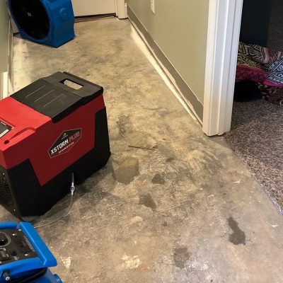 Dehumidifier and fans used during pipe break cleanup in a hallway with water damage.