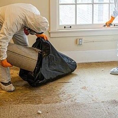 Two technicians in full protective gear performing trauma and crime scene cleanup in a residential home with proper safety protocols.